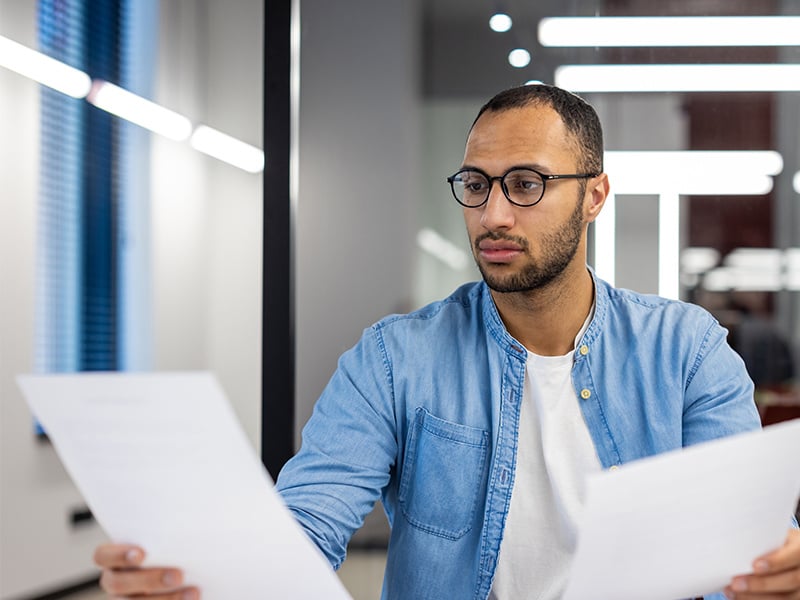 Male Employee Wearing Glasses In Blue Shirt Loooking At Reports